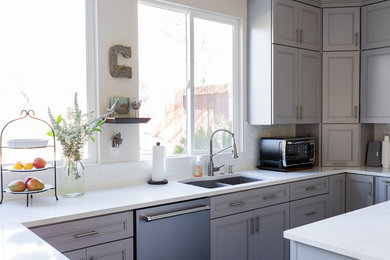 Modern inredning av ett mellanstort vit vitt kök, med en nedsänkt diskho, släta luckor, grå skåp, bänkskiva i kvarts, vitt stänkskydd, stänkskydd i keramik, rostfria vitvaror, laminatgolv, en köksö och brunt golv