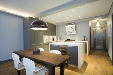 Medium sized modern l-shaped kitchen/diner in New York with a submerged sink, flat-panel cabinets, grey cabinets, composite countertops, white splashback, stainless steel appliances, light hardwood flooring, an island and brown floors.