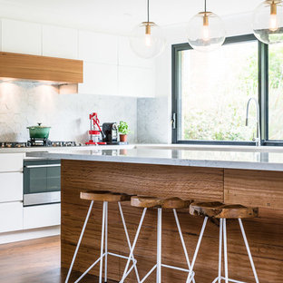 Photo of a contemporary kitchen in Sydney with flat-panel cabinets, white cabinets, grey splashback, medium hardwood floors, with island, brown floor and grey benchtop.