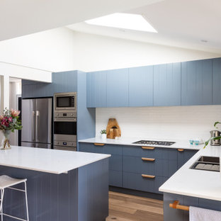 Design ideas for a mid-sized contemporary kitchen with blue cabinets, quartz benchtops, white splashback, porcelain splashback, stainless steel appliances, white benchtop, a double-bowl sink, medium hardwood floors and with island.
