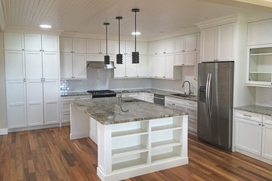 Large trendy l-shaped medium tone wood floor and brown floor kitchen photo in Other with an undermount sink, shaker cabinets, white cabinets, granite countertops, white backsplash, subway tile backsplash, stainless steel appliances and an island