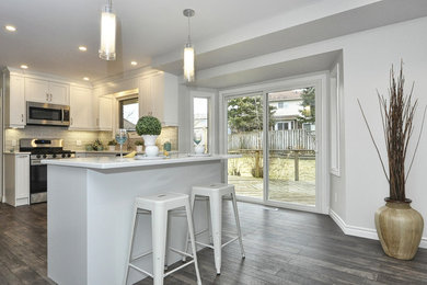 Example of a mid-sized minimalist l-shaped laminate floor and gray floor eat-in kitchen design in Other with an undermount sink, shaker cabinets, white cabinets, quartzite countertops, gray backsplash, porcelain backsplash, stainless steel appliances, an island and white countertops