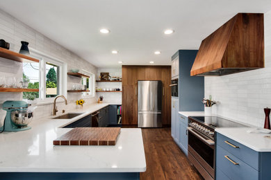 Inspiration for a mid-sized transitional l-shaped dark wood floor and brown floor eat-in kitchen remodel in Denver with a single-bowl sink, shaker cabinets, blue cabinets, quartz countertops, white backsplash, porcelain backsplash, stainless steel appliances, a peninsula and white countertops