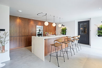 Foto di una cucina lineare moderna di medie dimensioni con ante lisce, ante in legno bruno, top in marmo, elettrodomestici da incasso, pavimento in cemento, penisola e pavimento grigio