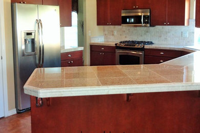 Inspiration for a mid-sized timeless u-shaped ceramic tile eat-in kitchen remodel in Boise with a drop-in sink, flat-panel cabinets, red cabinets, tile countertops, beige backsplash, stone tile backsplash and stainless steel appliances
