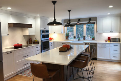 Inspiration for a large transitional u-shaped light wood floor eat-in kitchen remodel in Boston with a farmhouse sink, flat-panel cabinets, white cabinets, quartz countertops, white backsplash, subway tile backsplash, stainless steel appliances, an island and white countertops