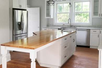 Inspiration for a mid-sized transitional l-shaped medium tone wood floor and red floor eat-in kitchen remodel in Boston with a farmhouse sink, shaker cabinets, white cabinets, quartzite countertops, white backsplash, stainless steel appliances and an island