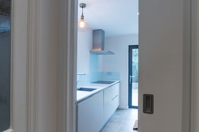 Photo of a medium sized contemporary galley enclosed kitchen in London with a built-in sink, flat-panel cabinets, white cabinets, composite countertops, blue splashback, glass sheet splashback, stainless steel appliances, porcelain flooring and no island.