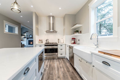 Large trendy u-shaped medium tone wood floor and brown floor eat-in kitchen photo in Vancouver with a farmhouse sink, shaker cabinets, white cabinets, white backsplash, subway tile backsplash, stainless steel appliances, an island and quartz countertops