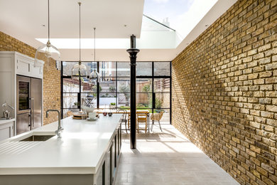 Diseño de cocina comedor clásica renovada de tamaño medio con fregadero integrado, armarios estilo shaker, puertas de armario grises, encimera de acrílico, electrodomésticos de acero inoxidable, suelo de piedra caliza y una isla