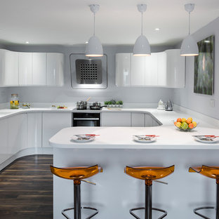 Medium sized modern u-shaped kitchen/diner in West Midlands with a built-in sink, white cabinets, white splashback, stainless steel appliances, dark hardwood flooring, a breakfast bar, brown floors, white worktops and flat-panel cabinets.
