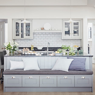 Imagen de cocina contemporánea con fregadero bajoencimera, armarios tipo vitrina, puertas de armario blancas, salpicadero blanco, salpicadero de azulejos tipo metro, suelo de madera clara, una isla, suelo beige y encimera de granito