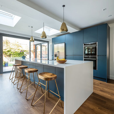 Example of a large trendy galley vinyl floor and brown floor open concept kitchen design in London with flat-panel cabinets, blue cabinets, quartzite countertops, stainless steel appliances, an island and white countertops