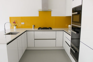 Design ideas for a medium sized contemporary kitchen/diner in Essex with white cabinets, quartz worktops, yellow splashback, glass sheet splashback and black appliances.