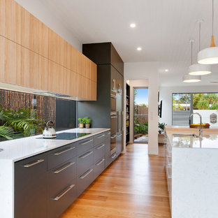 Inspiration for a large beach style galley open plan kitchen in Sunshine Coast with flat-panel cabinets, medium hardwood floors, multiple islands, brown floor, white benchtop, an undermount sink, window splashback and panelled appliances.