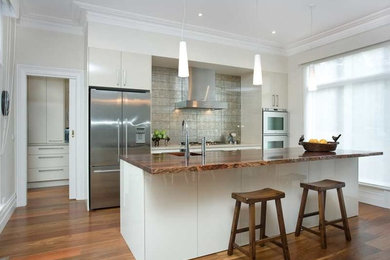 Photo of a medium sized modern single-wall kitchen pantry in Melbourne with a double-bowl sink, flat-panel cabinets, white cabinets, wood worktops, grey splashback, stone tiled splashback, stainless steel appliances, medium hardwood flooring and an island.