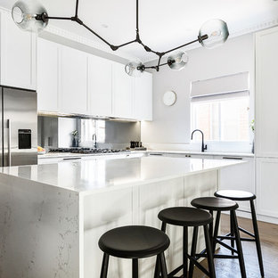 Design ideas for a large transitional l-shaped open plan kitchen in Sydney with an undermount sink, shaker cabinets, white cabinets, quartz benchtops, mirror splashback, medium hardwood floors, with island, brown floor, white benchtop and stainless steel appliances.