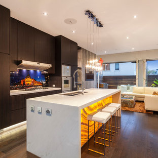 This is an example of a mid-sized contemporary single-wall open plan kitchen in Melbourne with flat-panel cabinets, dark wood cabinets, dark hardwood floors, with island, brown floor, a double-bowl sink, marble benchtops, multi-coloured splashback, glass sheet splashback, white appliances and white benchtop.