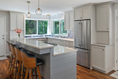 Large trendy l-shaped medium tone wood floor and brown floor open concept kitchen photo in Other with shaker cabinets, gray cabinets, quartz countertops, an island, gray countertops, an undermount sink, blue backsplash, subway tile backsplash and stainless steel appliances