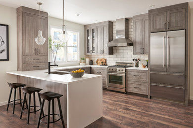 Large trendy u-shaped vinyl floor and brown floor open concept kitchen photo in Other with an undermount sink, shaker cabinets, gray cabinets, white backsplash, subway tile backsplash, stainless steel appliances and a peninsula
