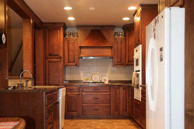Example of a mid-sized classic u-shaped ceramic tile and beige floor eat-in kitchen design in Denver with an undermount sink, raised-panel cabinets, brown cabinets, granite countertops, white backsplash, ceramic backsplash, white appliances, an island and brown countertops