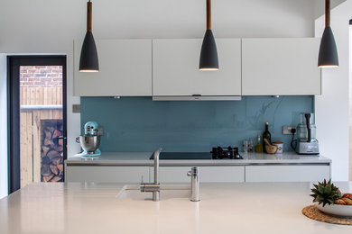 Inspiration for a large contemporary open plan kitchen in Surrey with flat-panel cabinets, white cabinets, quartz worktops, blue splashback, glass sheet splashback, medium hardwood flooring, stainless steel appliances and an island.