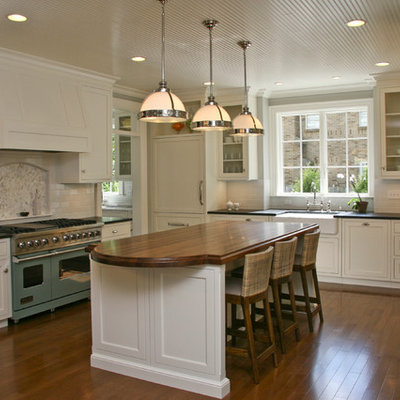 Large transitional l-shaped eat-in kitchen photo in Grand Rapids with a farmhouse sink, wood countertops, white cabinets, white backsplash, subway tile backsplash, colored appliances, recessed-panel cabinets and an island