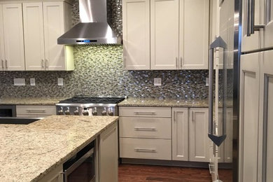 Example of a mid-sized classic u-shaped medium tone wood floor enclosed kitchen design in DC Metro with a farmhouse sink, shaker cabinets, white cabinets, granite countertops, multicolored backsplash, mosaic tile backsplash, stainless steel appliances and an island