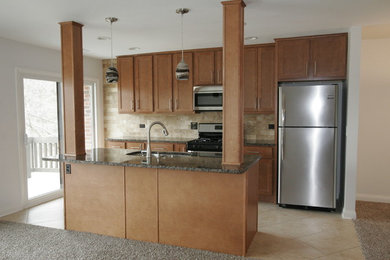 Photo of a medium sized galley kitchen/diner in Chicago with a submerged sink, granite worktops, beige splashback, stone tiled splashback, stainless steel appliances, ceramic flooring, an island, raised-panel cabinets and light wood cabinets.