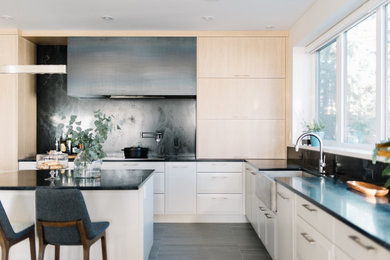 Eat-in kitchen - large contemporary l-shaped porcelain tile and gray floor eat-in kitchen idea in Edmonton with a farmhouse sink, flat-panel cabinets, white cabinets, quartz countertops, black backsplash, stone slab backsplash, stainless steel appliances, an island and black countertops