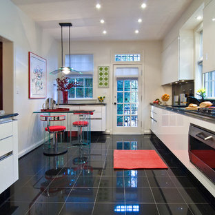Design ideas for a mid-sized modern galley eat-in kitchen in DC Metro with flat-panel cabinets, white cabinets, an undermount sink, black splashback, stone slab splashback, stainless steel appliances, marble floors, black floor, with island, granite benchtops and black benchtop.