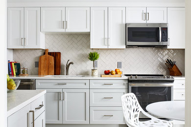 Modelo de cocina comedor clásica de tamaño medio con puertas de armario blancas, salpicadero blanco, salpicadero de azulejos tipo metro, electrodomésticos de acero inoxidable y suelo vinílico