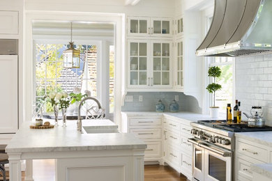 Example of a mid-sized classic u-shaped medium tone wood floor kitchen design in Seattle with glass-front cabinets, white cabinets, an island, a farmhouse sink, marble countertops, gray backsplash, ceramic backsplash and stainless steel appliances