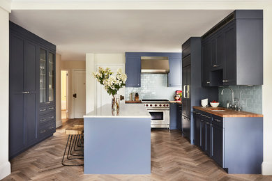 Inspiration for a large classic galley open plan kitchen in New York with a built-in sink, shaker cabinets, blue cabinets, marble worktops, blue splashback, ceramic splashback, stainless steel appliances, light hardwood flooring, an island and beige floors.