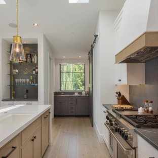 Coastal open concept kitchen ideas - Beach style u-shaped light wood floor open concept kitchen photo in Seattle with a single-bowl sink, recessed-panel cabinets, light wood cabinets, quartzite countertops, black backsplash, porcelain backsplash, two islands and black countertops