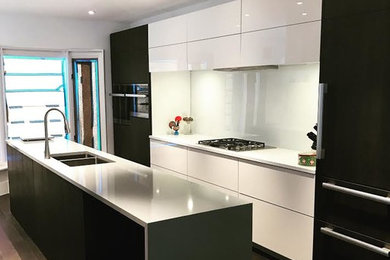 Mid-sized trendy galley dark wood floor and brown floor kitchen photo in Toronto with a double-bowl sink, flat-panel cabinets, white cabinets, solid surface countertops, glass sheet backsplash, paneled appliances and an island