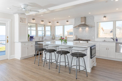 Mid-sized beach style u-shaped painted wood floor and brown floor eat-in kitchen photo in New York with an undermount sink, shaker cabinets, white cabinets, quartzite countertops, gray backsplash, marble backsplash, stainless steel appliances, an island and white countertops