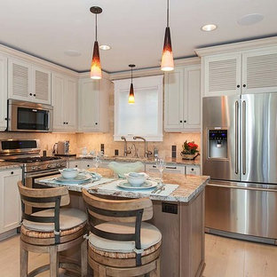 This is an example of a small beach style l-shaped open plan kitchen in Seattle with an undermount sink, louvered cabinets, white cabinets, granite benchtops, beige splashback, stone tile splashback, stainless steel appliances, porcelain floors and with island.