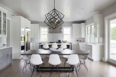 Photo of a large traditional u-shaped kitchen/diner in New York with white splashback, medium hardwood flooring, an island, a submerged sink, shaker cabinets, white cabinets, stainless steel appliances and white worktops.
