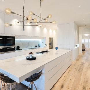 Photo of a contemporary eat-in kitchen in Adelaide with an undermount sink, flat-panel cabinets, white cabinets, white splashback, stainless steel appliances, light hardwood floors, with island, beige floor and white benchtop.