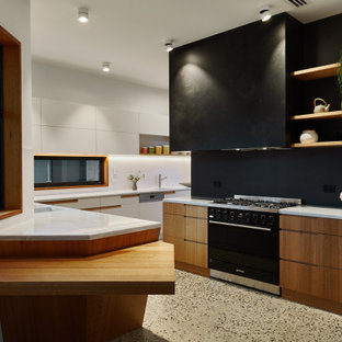 Design ideas for a large contemporary l-shaped kitchen in Adelaide with flat-panel cabinets, medium wood cabinets, white splashback, terrazzo floors, a peninsula, grey floor, white benchtop, a farmhouse sink, solid surface benchtops, ceramic splashback and black appliances.
