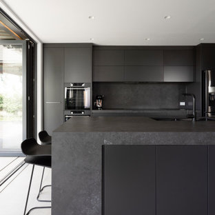 Inspiration for a mid-sized contemporary galley open plan kitchen in Sydney with an undermount sink, grey floor, grey cabinets, solid surface benchtops, grey splashback, stone slab splashback, black appliances, cement tiles, with island and grey benchtop.