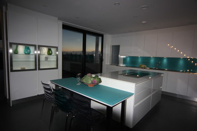 This is an example of a large nautical u-shaped kitchen/diner in Sussex with a single-bowl sink, flat-panel cabinets, white cabinets, quartz worktops, green splashback, glass sheet splashback, black appliances, ceramic flooring and an island.