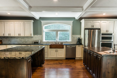 This is an example of a large traditional l-shaped kitchen/diner in Boston with a belfast sink, raised-panel cabinets, white cabinets, granite worktops, white splashback, stone tiled splashback, stainless steel appliances, light hardwood flooring and multiple islands.