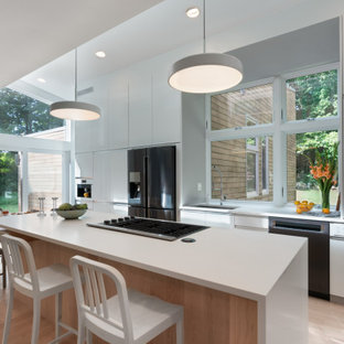 Mid-sized modern open concept kitchen ideas - Example of a mid-sized minimalist single-wall light wood floor open concept kitchen design in Boston with a single-bowl sink, flat-panel cabinets, white cabinets, quartz countertops, glass sheet backsplash, black appliances, an island and white countertops