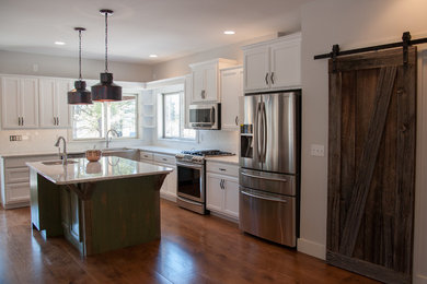 Mid-sized transitional l-shaped medium tone wood floor eat-in kitchen photo in Other with a farmhouse sink, raised-panel cabinets, white cabinets, granite countertops, white backsplash, subway tile backsplash, stainless steel appliances and an island