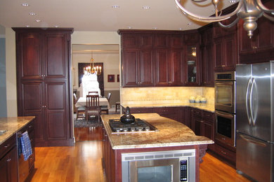 Example of a large transitional l-shaped medium tone wood floor eat-in kitchen design in New York with an undermount sink, raised-panel cabinets, dark wood cabinets, granite countertops, beige backsplash, porcelain backsplash, stainless steel appliances and an island