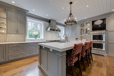Example of a transitional u-shaped medium tone wood floor eat-in kitchen design in Philadelphia with an undermount sink, recessed-panel cabinets, gray cabinets, marble countertops, white backsplash, stainless steel appliances and an island