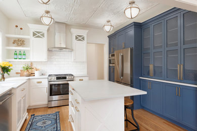 Photo of a beach style enclosed kitchen in Minneapolis with shaker cabinets, blue cabinets, white splashback, metro tiled splashback, stainless steel appliances, light hardwood flooring, an island and grey worktops.