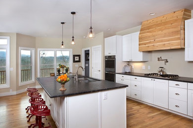 Inspiration for a large country l-shaped light wood floor and brown floor eat-in kitchen remodel in Other with an undermount sink, recessed-panel cabinets, white cabinets, soapstone countertops, beige backsplash, stainless steel appliances and an island